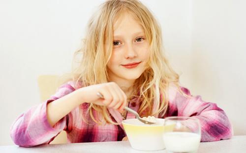 La ragazza con una faccia angelica mangia il porridge con piacere