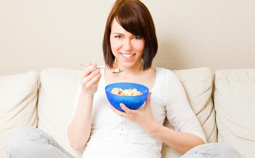 La ragazza sorride e mangia il porridge da una ciotola blu