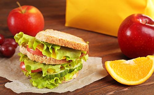 Panino con insalata verde, fetta d'arancia e mele rosse per la colazione