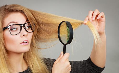 La bionda esamina i suoi capelli in una lente d'ingrandimento