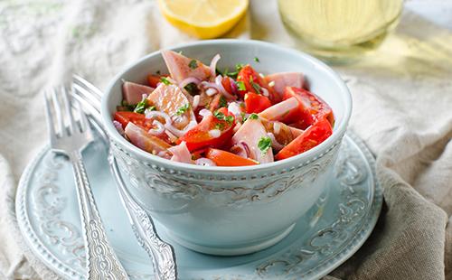 Una tazza di insalata con prosciutto e pomodori