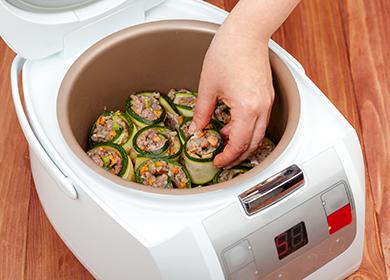 Una mano mette zucchine ripiene in una ciotola multicooker