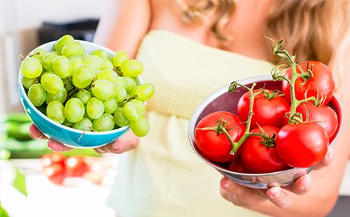 La donna tiene i pomodori e l'uva in tazze