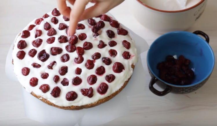 La prima torta è unta di panna e distribuisce uniformemente le ciliegie su di essa.