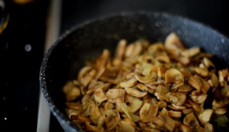 Friggere i funghi con le cipolle in una padella fino a cottura.