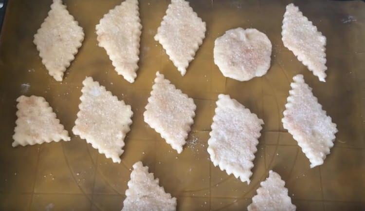 Distribuiamo i biscotti su una teglia coperta di carta da forno, dopo aver immerso ogni pezzo in una miscela di cannella e zucchero.