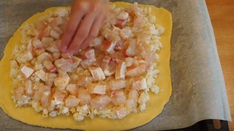 Distribuiamo uno strato di pasta su una teglia, su di esso livelliamo il riso con le cipolle e sopra di esso spalmiamo il pesce.