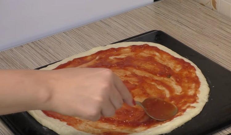 Lubrificare la base per pizza con salsa di pomodoro.