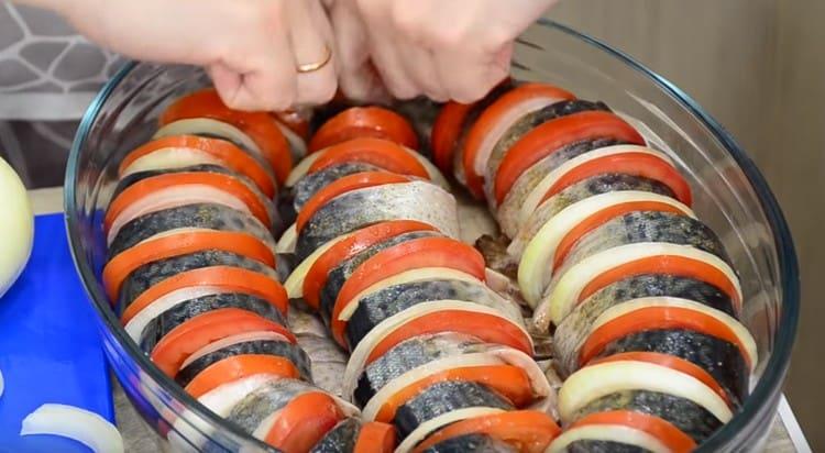 In una forma unta con olio vegetale, stendi i pezzi di pesce, alternandoli con fette di cipolle e pomodori.