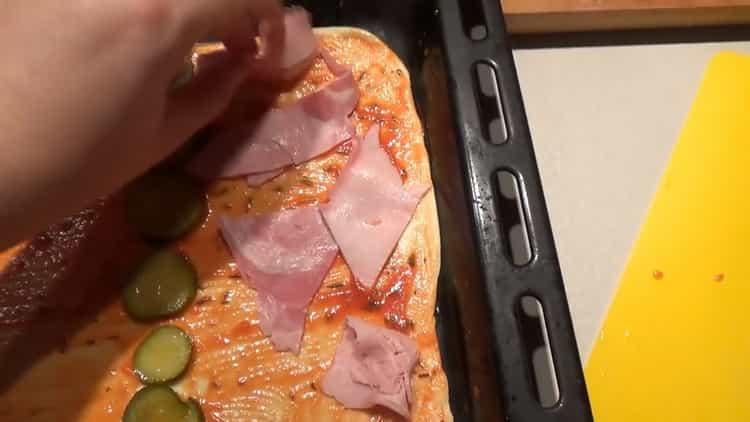 Per preparare i condimenti per la pizza, metti il ​​prosciutto sull'impasto