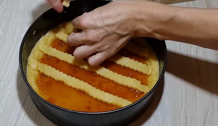 Per preparare una torta di pasta frolla con marmellata, metti le strisce di pasta sul ripieno