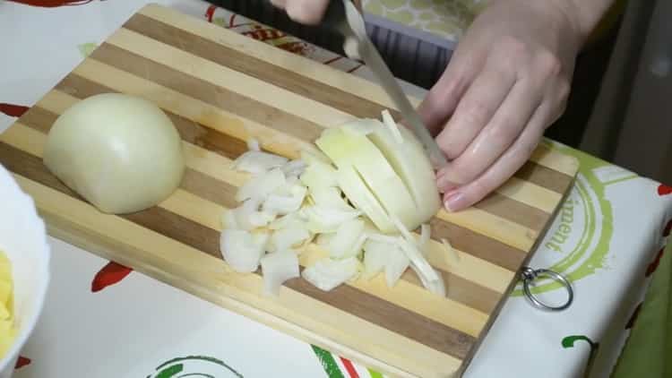 Per fare una torta con pesce e patate, trita la cipolla