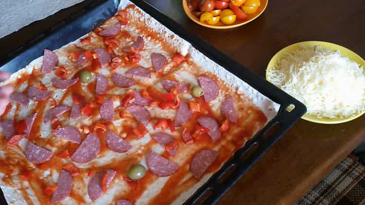 Per cuocere la pizza dal pane pita nel forno, tagliare la salsiccia