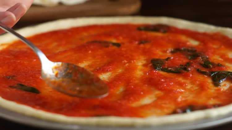 Per preparare la pizza margarita, ungere l'impasto con la salsa