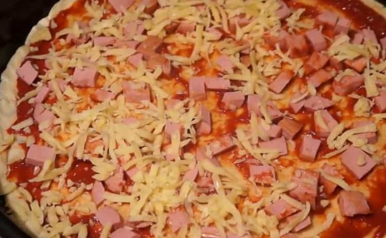 Per fare la pizza con salsiccia e formaggio, metti il ​​ripieno sull'impasto