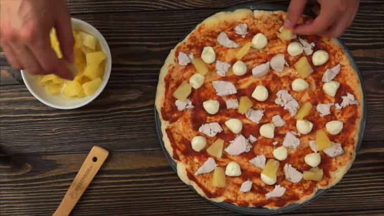 Per preparare la pizza con pollo e ananas, adagiare il ripieno sulla base