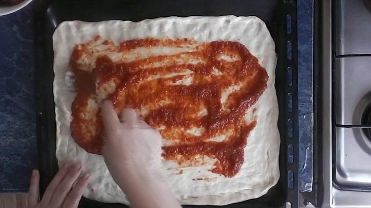 Per fare la pizza con sottaceti, ungere l'impasto con ketchup