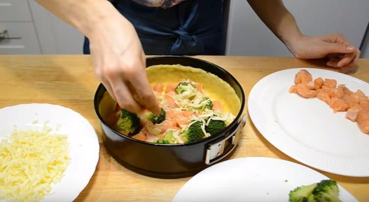 Distribuiamo metà del pesce e dei broccoli sull'impasto, cospargendo con un pezzo di formaggio.