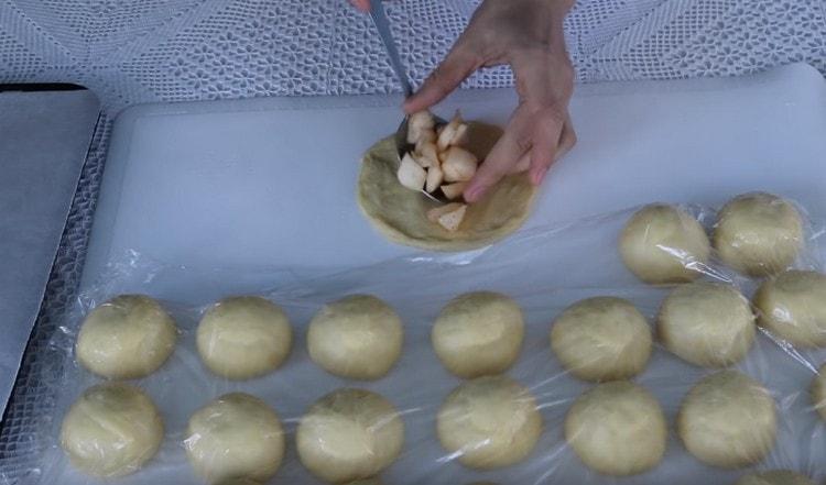 Impastare ogni pallina di pasta con una mano in una torta e mettere il ripieno di mele al centro.