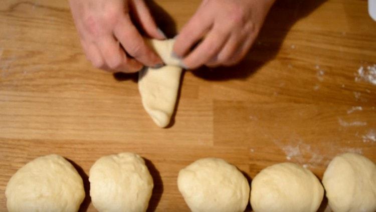 Rotoliamo ogni pallina in una lunga torta, la pieghiamo a metà e la arrotoliamo.