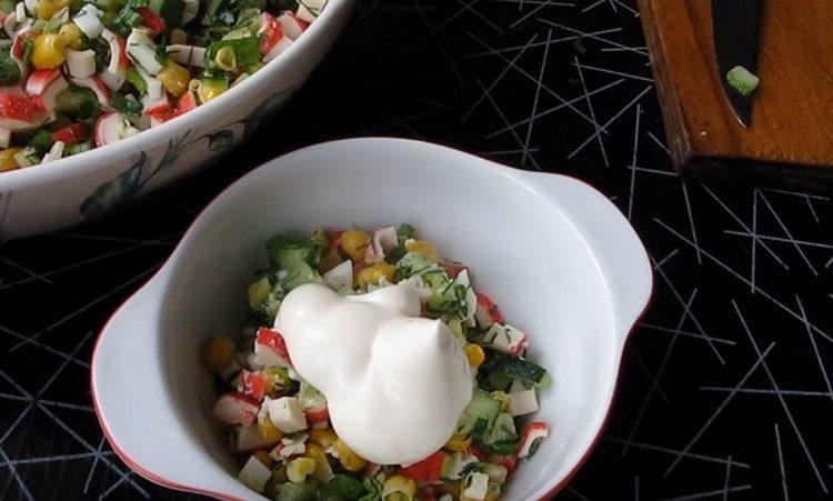 Condire l'insalata con bastoncini di granchio, mais, uova e cetriolo con maionese.