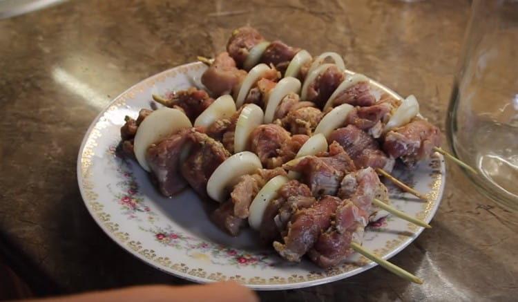 Stringiamo la carne alternativamente con cipolle su spiedini di legno.