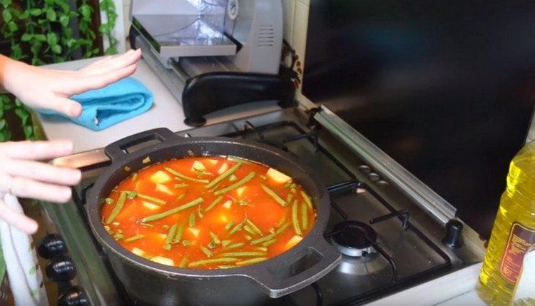 Aggiungere patate e fagioli al calderone, versare acqua, aggiungere sale, pepe e piselli e stufare il piatto.