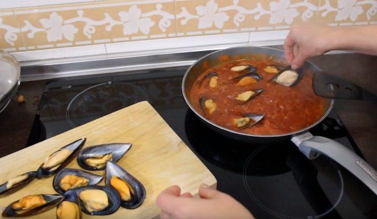 Distribuiamo le cozze in salsa di pomodoro e cuociamo a fuoco lento per alcuni minuti sotto il coperchio.